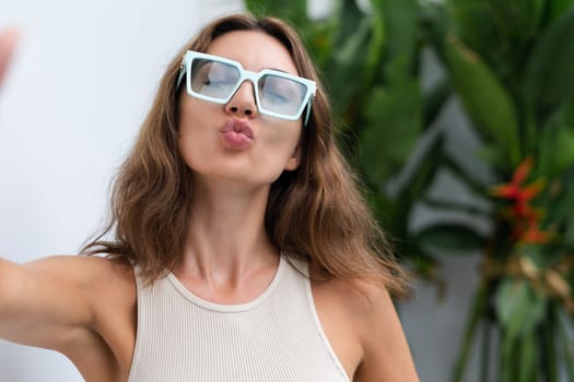 Stylish fit fashion women in trendy mint sunglasses posing at luxury tropical villa outdoor natural day light doing selfie blow a kiss to camera