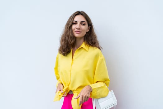 Stylish fit fashion women in yellow shirt and bright pink pants holding bag trendy posing on white wall background outdoor natural day light