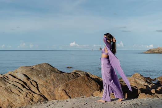 Young beautiful woman in a romantic mood, lilac silk clothes, on the beach against the backdrop of the sea and stones at sunset