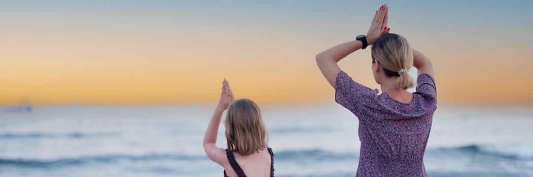 Mother and daughter do yoga on beach in evening. People have fun outdoors. Concept of summer holidays and friendly family and relaxation.