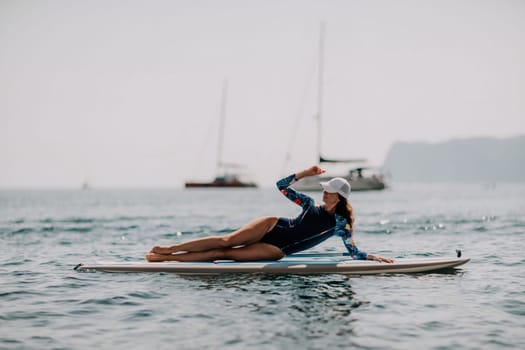 Woman sup yoga. Middle age sporty woman practising yoga pilates on paddle sup surfboard. Female stretching doing workout on sea water. Modern individual hipster outdoor summer sport activity