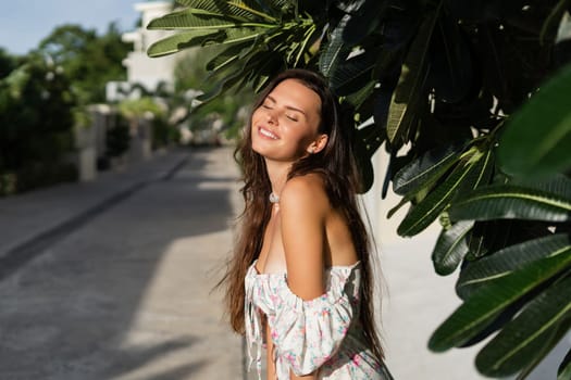 Young beautiful woman in a romantic dress with a floral print, and a pearl necklace bracelet, against the backdrop of tropical leaves