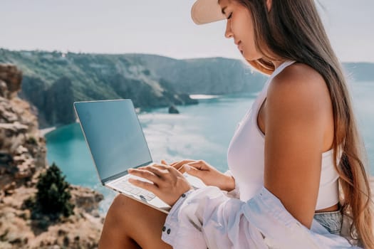 Digital nomad, Business woman working on laptop by the sea. Pretty lady typing on computer by the sea at sunset, makes a business transaction online from a distance. Freelance remote work on vacation