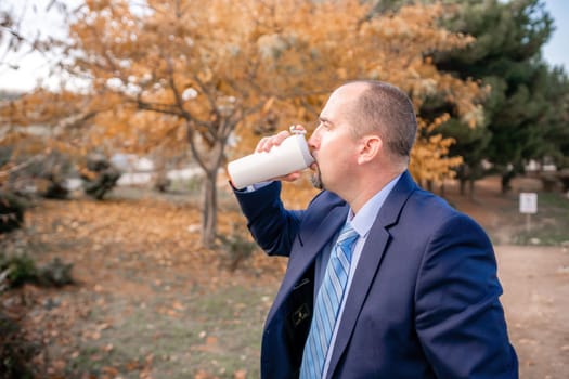 Mature entrepreneur drink coffee in autumn park. Senior executive rest in city park.