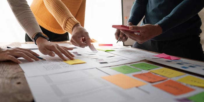 Close up ux developer and ui designer brainstorming about mobile app interface wireframe design on table with customer brief and color code at modern office.Creative digital development agency.panning.