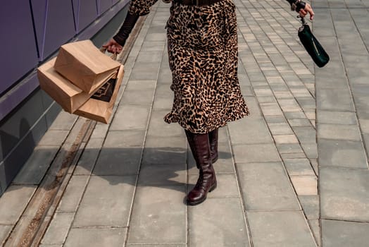 A happy shopaholic girl keeps her bags near the shopping center. A woman near the store is happy with her purchases, holding bags. Dressed in a leopard print dress. Consumer concept