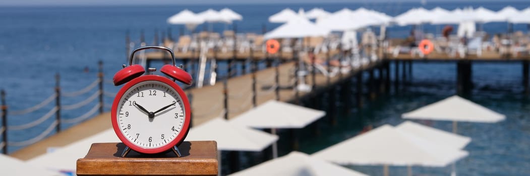 Alarm clock for ten o'clock on beach with jetty and umbrellas. Summer vacation time tourism and travel to sea