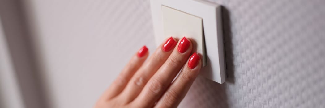 Female hand presses white switch on gray wall closeup. Saving electricity at home concept