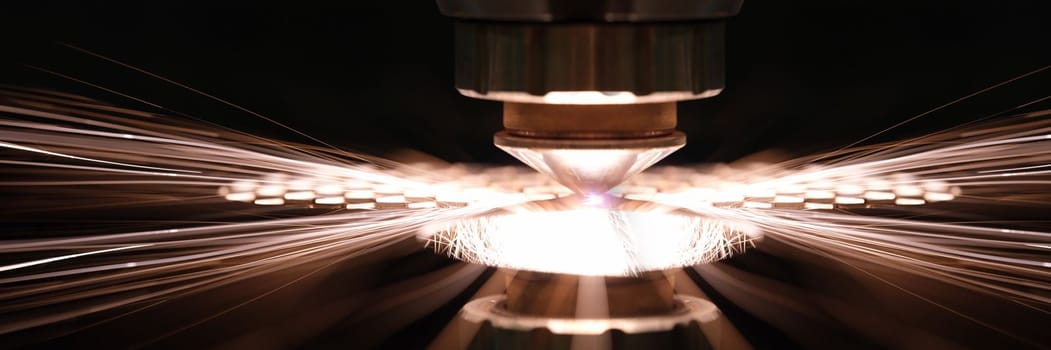 Laser cutting of metal sheet in production closeup. Sparks fly out machine head for metal processing