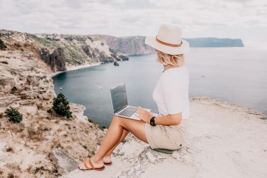 Digital nomad, Business woman working on laptop by the sea. Pretty lady typing on computer by the sea at sunset, makes a business transaction online from a distance. Freelance remote work on vacation