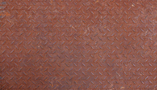 Background texture of rusty corroded weathered industrial anti slip embossed metal steel plate surface with diagonal bumps of diamond pattern, close up