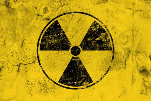 Black radioactive hazard warning sign painted over grunge yellow background with copy space