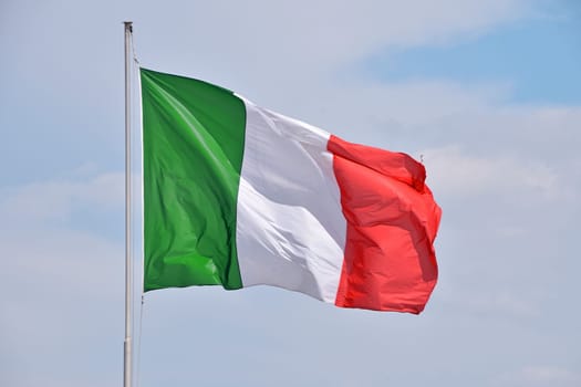 National flag of Italy flying and waving in the wind on flagstaff over clear blue sky, symbol of Italian patriotism, low angle, side view