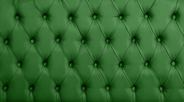 Close up background texture of dark green capitone genuine leather, retro Chesterfield style soft tufted furniture upholstery with deep diamond pattern and buttons