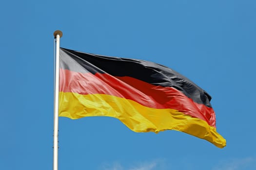 National flag of Germany flying and waving in the wind on flagstaff over clear blue sky, symbol of German patriotism, low angle, side view