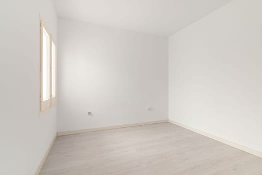 View of an empty white bright room with window without furniture after painting and renovation with wooden floor and baseboards. Concept of beautiful laconic interior for various inspiring ideas.