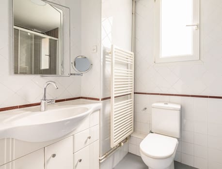 Cozy bright white bathroom with diamond shaped tiles with a window for natural light toilet sink and heated towel rail and mirror. Concept of modern cozy bathroom.