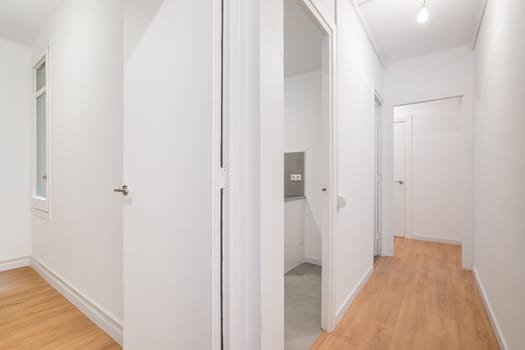 View from the entrance to new empty apartment after renovation in white tones with wooden floor. Cozy apartment in new building with modern minimalist design from the developer.