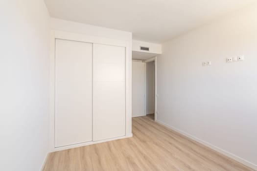 White empty sunny room with built-in wardrobe ventilation and two doors to the bathroom and exit. Concept of a new building or real estate for rent.