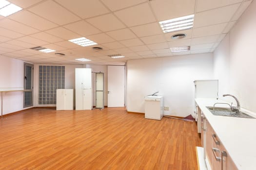 Old empty room with white kitchen furniture and sink that used to serve as office canteen for employees. A spacious and bright room, equipped as corporate dining room, needs new and fresh renovation