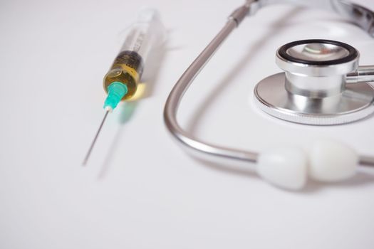 syringe, stethoscope and pills on a doctor's gown white background and copy space