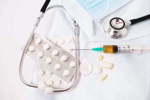 syringe, stethoscope and pills on a doctor's gown white background and copy space