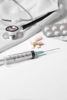 syringe, stethoscope and pills on a doctor's gown white background and copy space