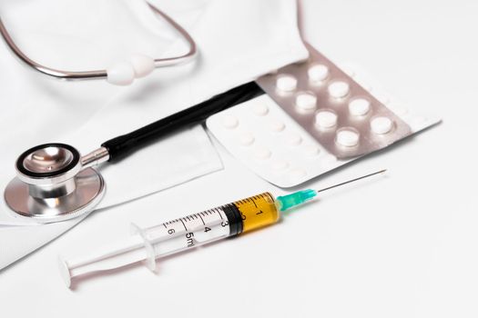 syringe, stethoscope and pills on a doctor's gown white background and copy space