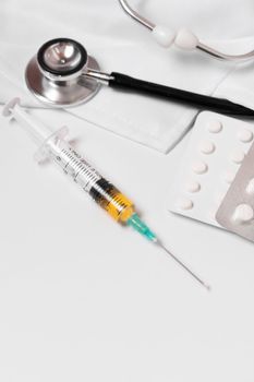 syringe, stethoscope and pills on a doctor's gown white background and copy space