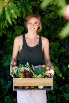 I choose organic produce. A young woman holding a crate of vegetables outdoors