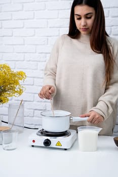 Creative hobby at home. Woman making decorative aroma candle at table, stirring melting soy wax in the pot