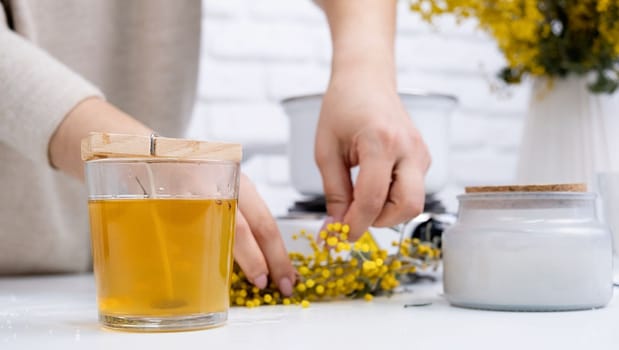 Creative hobby at home. Woman making decorative aroma candle with mimosa flowers at table