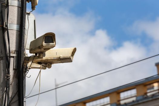two old security surveillance cameras on street light pole on blue sky background.