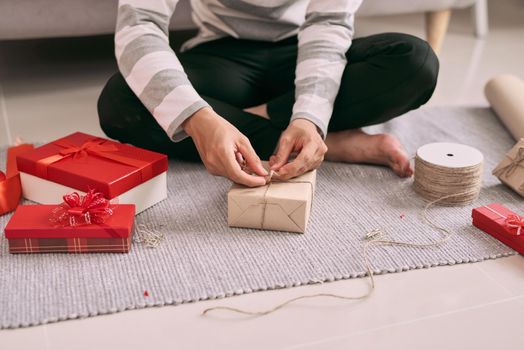 Young happy man packing Valentine gift while sitting on floor