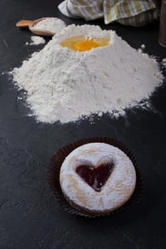 Pastry cookie with a red jam heart and icing powder sugar and cooking utensils on table