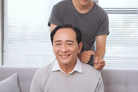 Son massaging father shoulder, sitting on sofa.