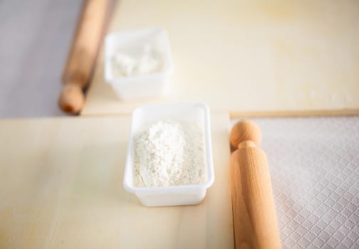 Wooden rolling pin with white wheat flour on the table