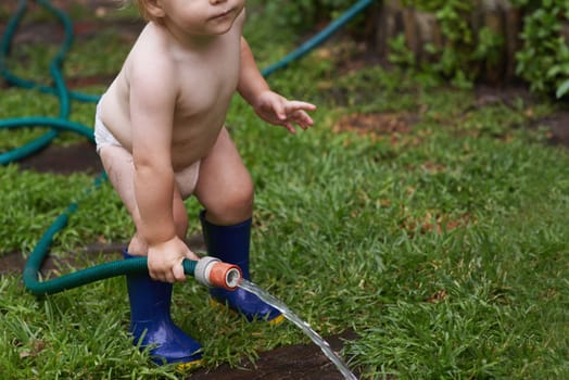 Hosepipe horseplay. A young toddler standing outside playing with a hosepipe
