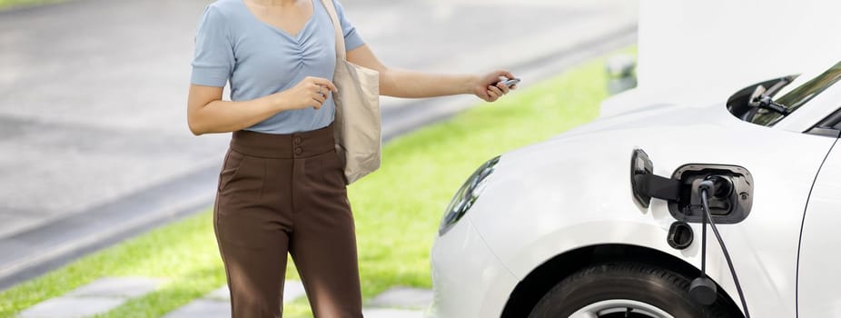 Closeup progressive woman install cable plug to her electric car with home charging station. Concept of the use of electric vehicles in a progressive lifestyle contributes to clean environment.