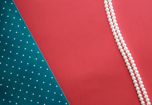 Pearl jewellery necklace and abstract blue polka dot background on coral backdrop.