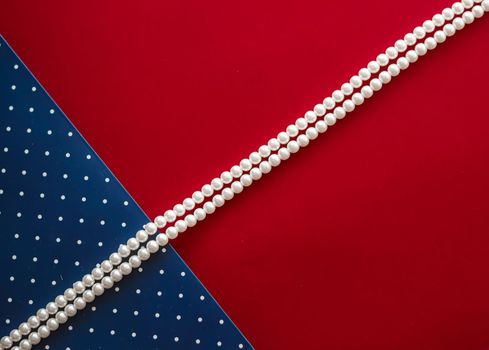 Pearl jewellery necklace and abstract blue polka dot background on red backdrop.