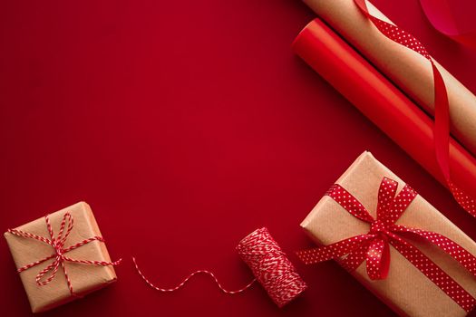 Gifts preparation, birthday and holidays gift giving, craft paper and ribbons for gift boxes on red background as wrapping tools and decorations, diy presents as holiday flat lay design.