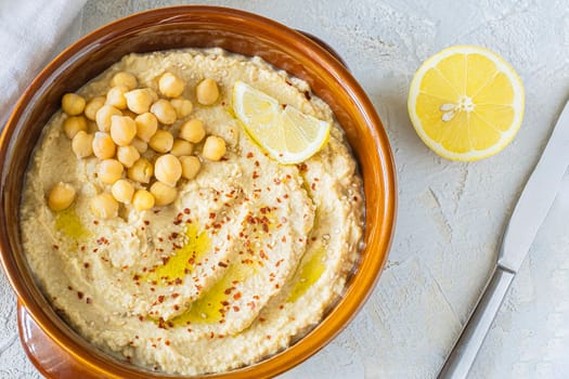 Home made hummus bowl, decorated with boiled chickpeas, olive oil, lemon on a light background. Top View. Copy space