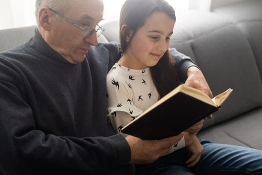 Happy little girl with grandfather reading story book at home.