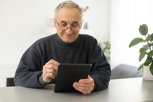 Smiling senior man reading news on digital tablet. Cheerful excited mature male using portable computer at home, copy space