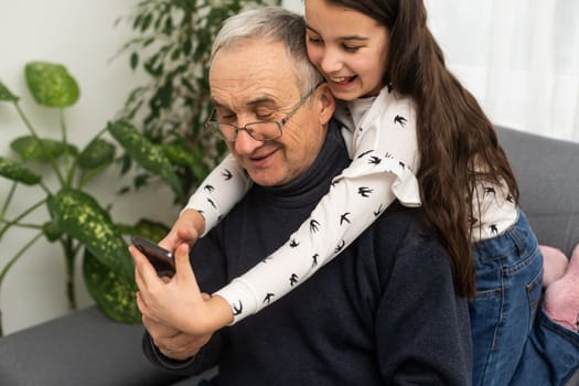 Teenage girl taking photo with mobile phone of herself and her grandfather