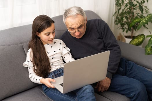 Happy retirement grandfather and pretty granddaughter laughing while watching e-book for learning to education together by laptop. Family educational at home concept. Technology and education