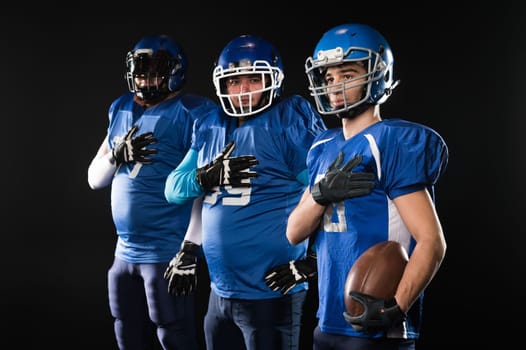 Portrait of three men in blue uniforms for American football with a hand on his chest on a black background