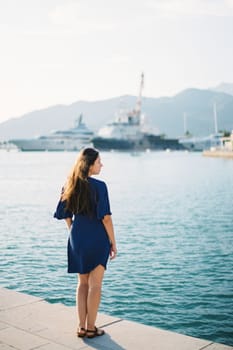 Young woman stands on the pier and looks at the ships. Back view. High quality photo