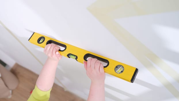 Hands of worker hold yellow level against white wall. Home craftsman and the evenness of walls concept